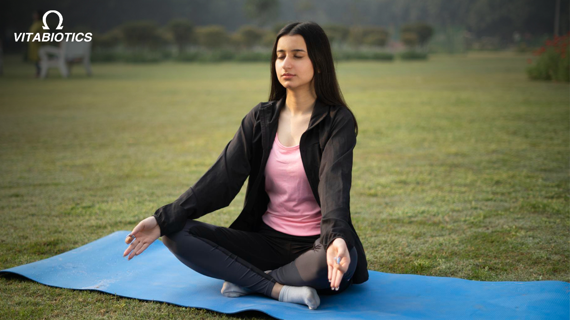 Woman meditating outdoors on yoga mat - Vitabiotics wellness.